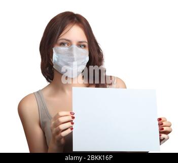 Une belle jeune femme de race blanche porte un masque facial et tient une feuille de papier vide dans ses mains pendant la pandémie de Covid 19 ou l'infection à coronavirus Banque D'Images