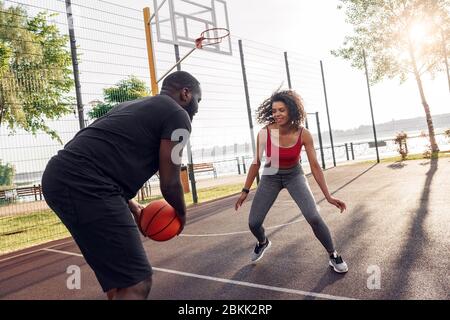 Activités en plein air. Couple africain jouant au basket-ball sur le terrain dribbling souriant excité Banque D'Images