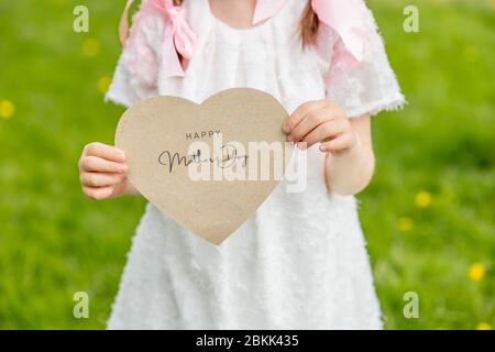 Bonne fête des mères écrit sur une carte en forme de coeur tenue par une fille sur fond d'herbe Banque D'Images