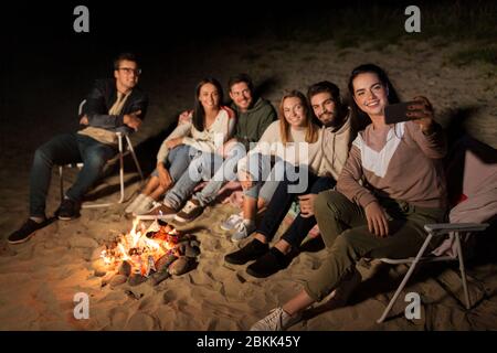 des amis heureux prenant le selfie au feu de camp sur la plage Banque D'Images