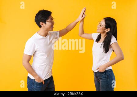 Image d'un homme et d'une femme multinational souriant dans des lunettes donnant cinq hautes isolées sur fond jaune Banque D'Images