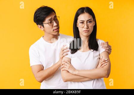 Image d'un homme asiatique mécontent embrassant une jeune femme pleine de ressentiment isolée sur fond jaune Banque D'Images