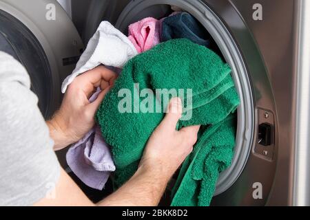 Homme prenant des vêtements de couleur de la machine à laver. Un tambour de lave-linge plein de linge sale dans la salle de bains. Banque D'Images