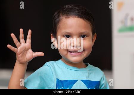 Un garçon de quatre ans utilisant ses doigts pour faire des gestes en coutant au numéro cinq et en souriant. Banque D'Images