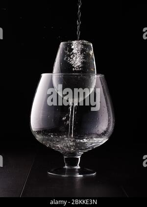 Verre à vin dans un verre à vin plus grand isolé sur fond noir se remplissant d'eau Banque D'Images