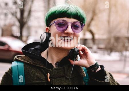 Portrait de happy non binaire hipster dans des lunettes de soleil violettes debout en ville Banque D'Images