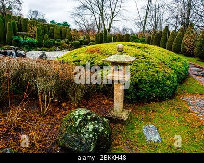 Vue sur une lanterne traditionnelle en pierre, ishi-doro ou ikekomi-doro, entourée de rochers décoratifs et de buissons dans un jardin japonais à Bonn, en Allemagne. Banque D'Images