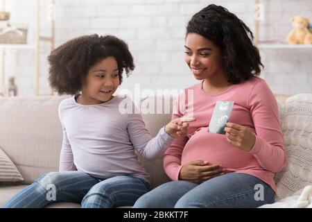 Petite fille noire regardant la photo d'échographie dans les mains de la mère enceinte Banque D'Images