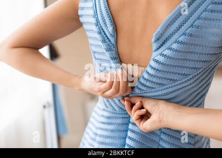 Femme essayant de se mettre en robe à fermeture à glissière debout à la maison, court Banque D'Images