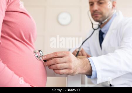 Homme médecin expérimenté examinant jeune femme enceinte Banque D'Images