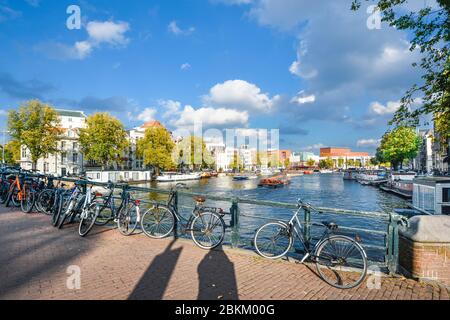 Le parc de vélos se trouve le long d'un pont sur l'un des plus grands canaux du centre historique d'Amsterdam, tandis qu'un bateau touristique se déplace au loin Banque D'Images