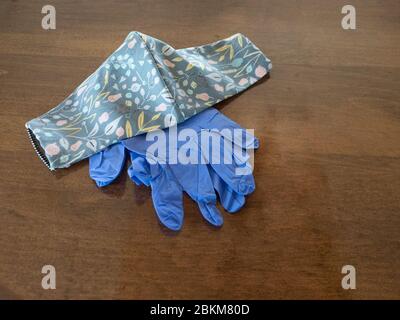 Paire de gants jetables bleus et un masque en tissu fait main avec motif floral gris sur une table en bois. Banque D'Images