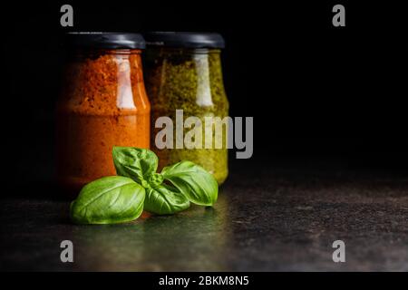 Basilic vert et pesto de tomates rouges trempent la sauce dans le bol et les feuilles de basilic sur la table noire. Banque D'Images