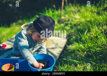 Un petit garçon d'âge préscolaire est la plantation de graines dans des pots à l'extérieur dans le jardin une journée de printemps Banque D'Images