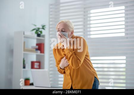 Femme dans un masque de protection toussant couvrant ses yeux. Banque D'Images