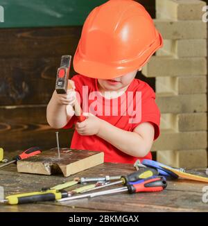 Enfant jouant avec un marteau. Casque orange couvrant le visage des garçons. Petit constructeur en atelier. Banque D'Images