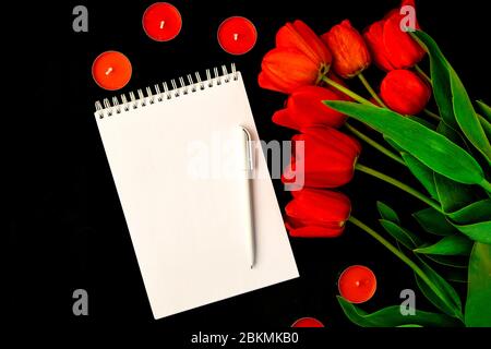 Tulipes rouges, carte vierge ou bloc-notes avec stylo et bougies isolées sur fond noir, espace de copie pour le texte Banque D'Images