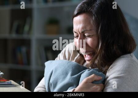 Triste femme adulte pleurant lamenter tenant un oreiller assis sur le sol la nuit à la maison Banque D'Images