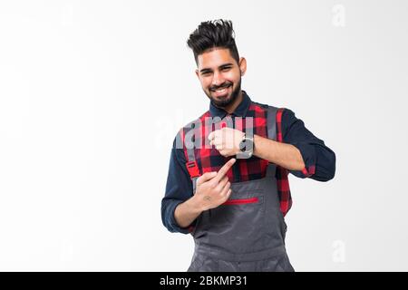 Nous faisons ontime. Jeune homme avec barbe dans l'ensemble bleu et t-shirt rouge debout et montrant le temps sur sa montre de poignet isolée sur fond blanc Banque D'Images