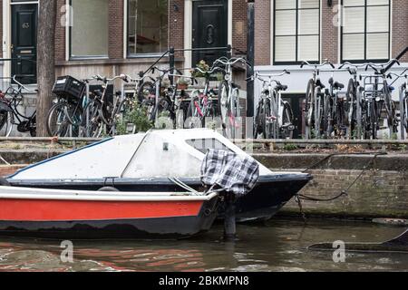 Vélos stationnés le long d'un canal avec des bateaux flottant à proximité, capturant la vie urbaine et le transport durable à Amsterdam. Banque D'Images