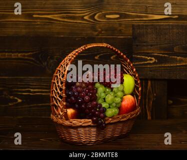 Panier rempli de fruits d'automne maison sur fond de bois vintage. Raisins et pommes dans un panier en osier. Concept de récolte et de jardinage. Banque D'Images