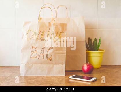 Sac en papier avec inscription - Sac en ligne, pomme rouge fraîche, téléphone mobile et une maison dans un pot jaune sur une table de cuisine. Achats en ligne et de contenu Banque D'Images