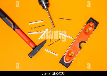 Outils de réparation pour l'utilisation à domicile. Marteau pour clous, niveau et foret, cheville dans le mur sur un fond orange. Boîte à outils de l'assistant Banque D'Images