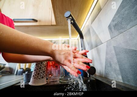 La fille se lave les mains sous l'eau courante dans un lavabo noir. Robinet d'eau, vaisselle propre, meubles de cuisine en bois Banque D'Images