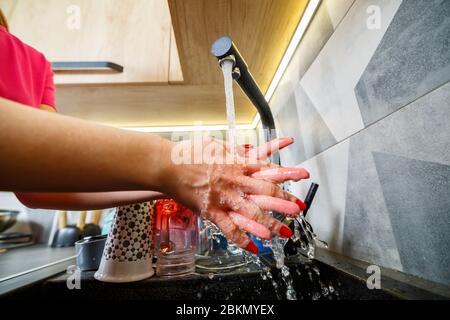 La fille se lave les mains sous l'eau courante dans un lavabo noir. Robinet d'eau, vaisselle propre, meubles de cuisine en bois Banque D'Images