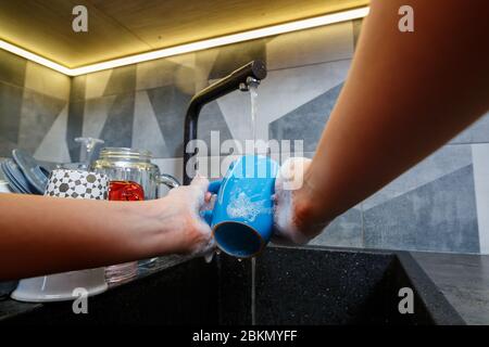 Mains avec éponge laver la tasse sous l'eau, femme de ménage dans le mug bleu dans un évier de cuisine avec une éponge bleue, nettoyage des mains, manuellement, housewo Banque D'Images