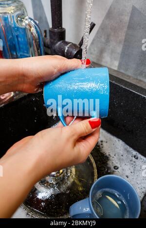 Mains avec éponge laver la tasse sous l'eau, femme de ménage dans le mug bleu dans un évier de cuisine avec une éponge bleue, nettoyage des mains, manuellement, housewo Banque D'Images