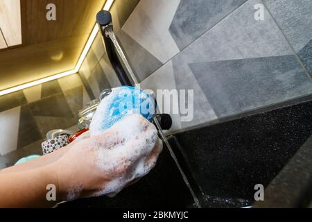 Mains avec éponge laver la tasse sous l'eau, femme de ménage dans le mug bleu dans un évier de cuisine avec une éponge bleue, nettoyage des mains, manuellement, housewo Banque D'Images