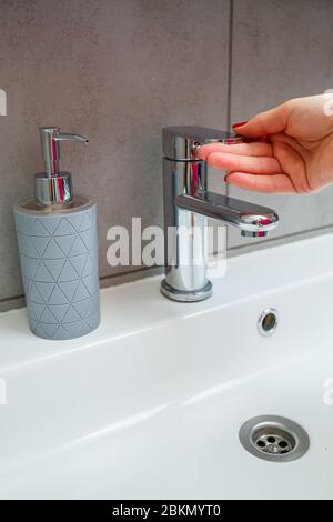 Lavabo blanc avec robinet en argent dans la salle de bains. CAN gris avec savon liquide pour les mains. Activation de l'eau du robinet, hygiène personnelle des mains Banque D'Images