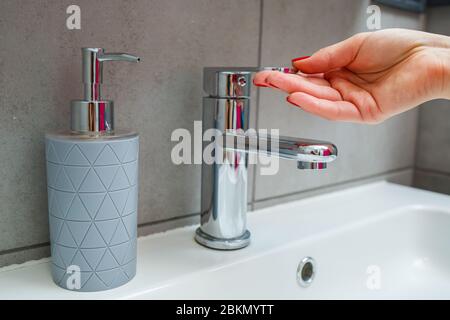 Lavabo blanc avec robinet en argent dans la salle de bains. CAN gris avec savon liquide pour les mains. Activation de l'eau du robinet, hygiène personnelle des mains Banque D'Images