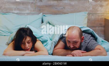 Jeune couple qui pose dans un lit portant un pyjama en conversation. Banque D'Images