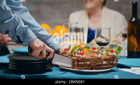 Gros plan d'une jeune femme qui coupe un délicieux gâteau à son anniversaire pour la famille. Banque D'Images