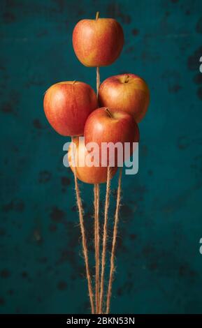 Bouquet de pommes rouges mûres flottant verticalement comme des ballons sur des fils de jute sur fond bleu flou Banque D'Images