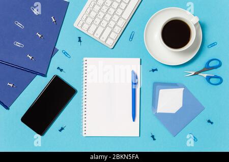 Espace de travail créatif avec clavier, tasse à café, bloc-notes, stylo, téléphone portable, enveloppe, ciseaux, épingles et clips en bleu et blanc. Concept de bureau à domicile. B Banque D'Images