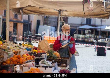 Le vendeur portant un masque protecteur sert un client sur le marché des fruits et légumes à Campo dei Fiori à Rome, Italie, le lundi 4 mai 2020. Banque D'Images