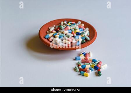 Un petit bol rempli de capsules médicales de couleur différente, quelques capsules séparées, affichées sur une table blanche Banque D'Images