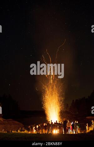 Les gens se rassemblent autour d'un feu de joie au bord d'une crique, avec des étoiles visibles et des lignes de lignes d'étincelles qui volent vers le haut, à Vinalhaven, Maine, Etats-Unis Banque D'Images