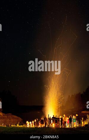 Les gens se rassemblent autour d'un feu de joie au bord d'une crique, avec des étoiles visibles et des lignes de lignes d'étincelles qui volent vers le haut, à Vinalhaven, Maine, Etats-Unis Banque D'Images