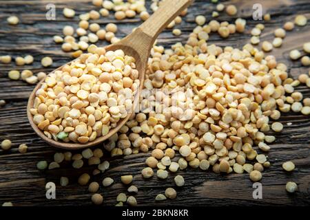 Pois jaunes secs dans une cuillère en bois brun sur un arrière-plan. Les haricots pour soupe nutritive Banque D'Images