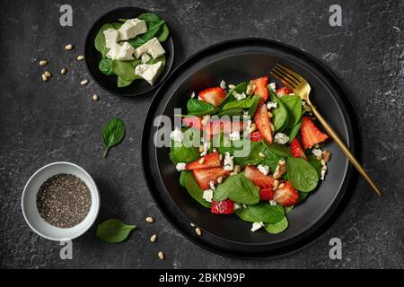 Vue de dessus d'une assiette noire avec salade d'épinards et de fraises et ses ingrédients Banque D'Images