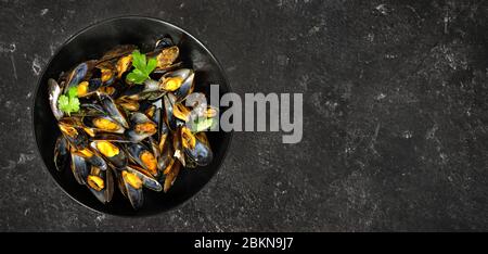 Vue de dessus des moules fraîchement cuites dans une assiette noire sur fond sombre Banque D'Images