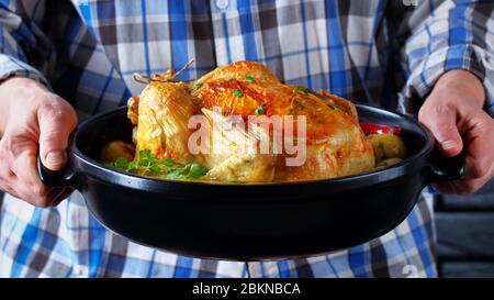 une femme porte un braiser en céramique noire avec du poulet rôti entier et une peau croustillante, en gros plan Banque D'Images