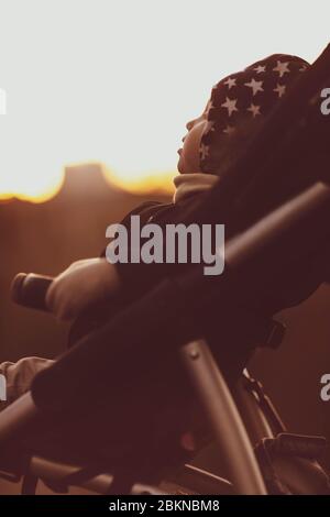 Un enfant dans un pram noir au coucher du soleil en automne. Banque D'Images