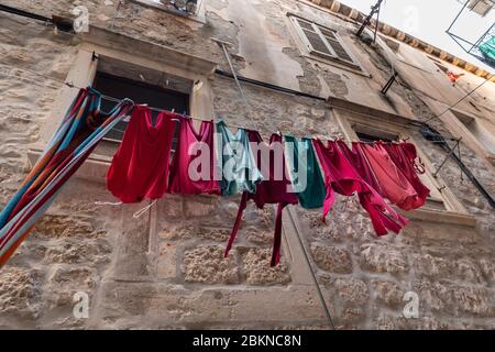 Blanchisserie fraîche avec différents vêtements colorés en bleu et rose accrochés devant un vieux mur rustique typique de la méditerranée dans la vieille ville de Dubrovnik Banque D'Images