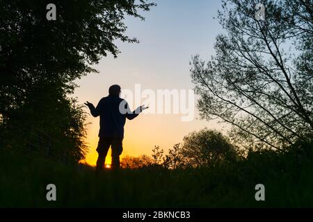 Homme avec ses bras levé marchant le long d'un chemin de halage à côté du canal d'oxford au lever du soleil. Oxfordshire, Angleterre. Silhouette Banque D'Images