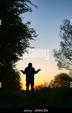 Homme avec ses bras levé marchant le long d'un chemin de halage à côté du canal d'oxford au lever du soleil. Oxfordshire, Angleterre. Silhouette Banque D'Images